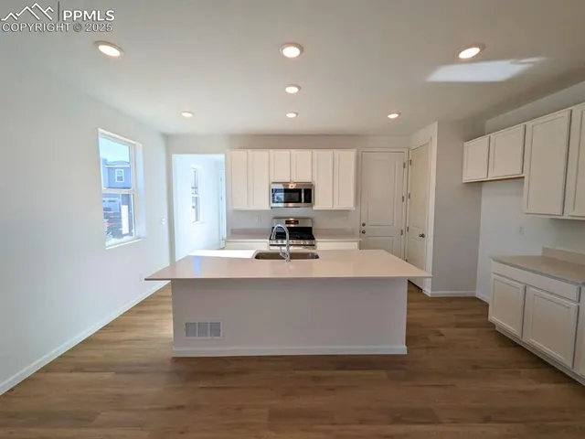a view of kitchen with stainless steel appliances granite countertop a stove a sink a refrigerator and white cabinets with wooden floor