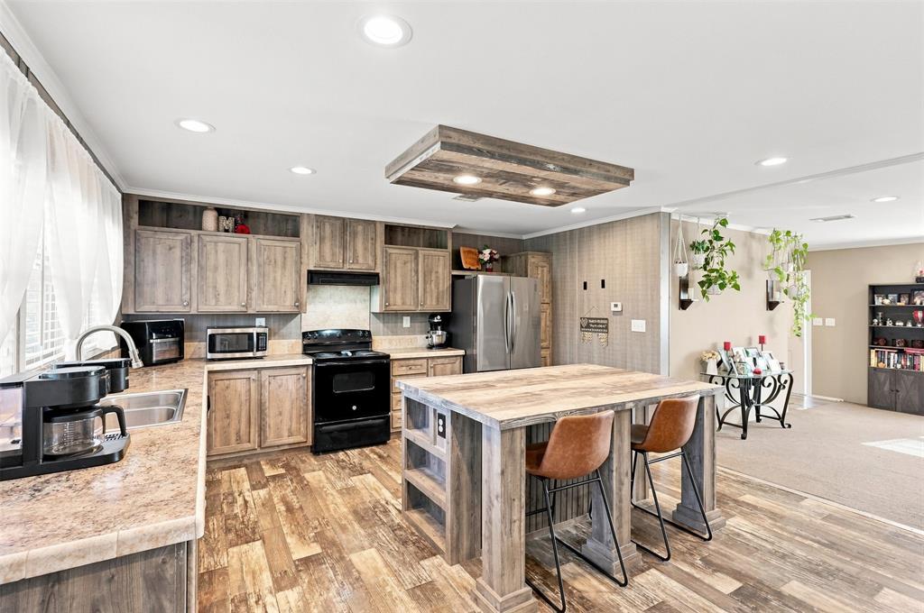 Spacious kitchen featuring wood-finish flooring, wood cabinetry, stone-look countertops, and a central island with integrated storage