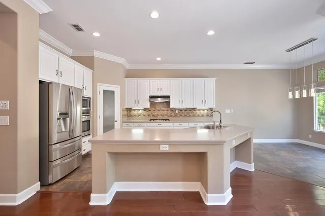 a kitchen with stainless steel appliances granite countertop a refrigerator a stove and white cabinets with wooden floors