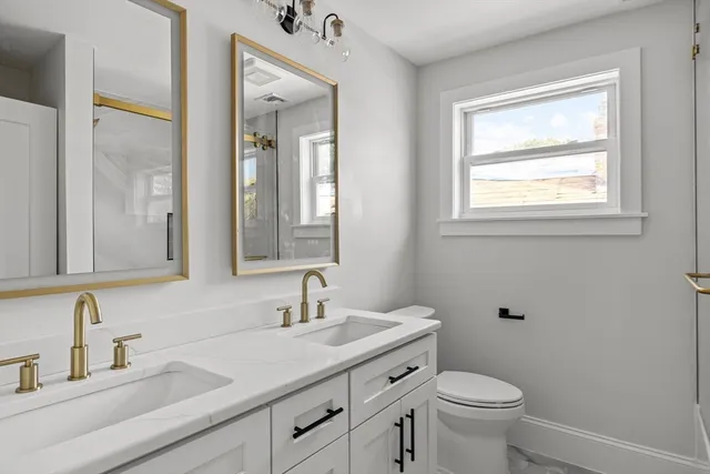 a bathroom with a granite countertop toilet a sink a mirror and a window
