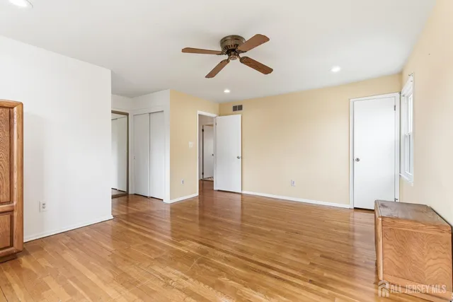 a view of an empty room with wooden floor and a ceiling fan
