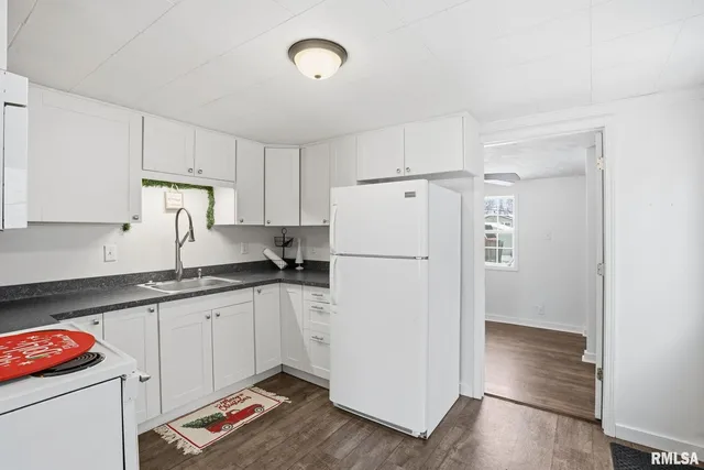 a kitchen with granite countertop a refrigerator a sink and white cabinets