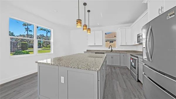 a kitchen with stainless steel appliances a refrigerator a sink dishwasher a stove and white cabinets with wooden floor