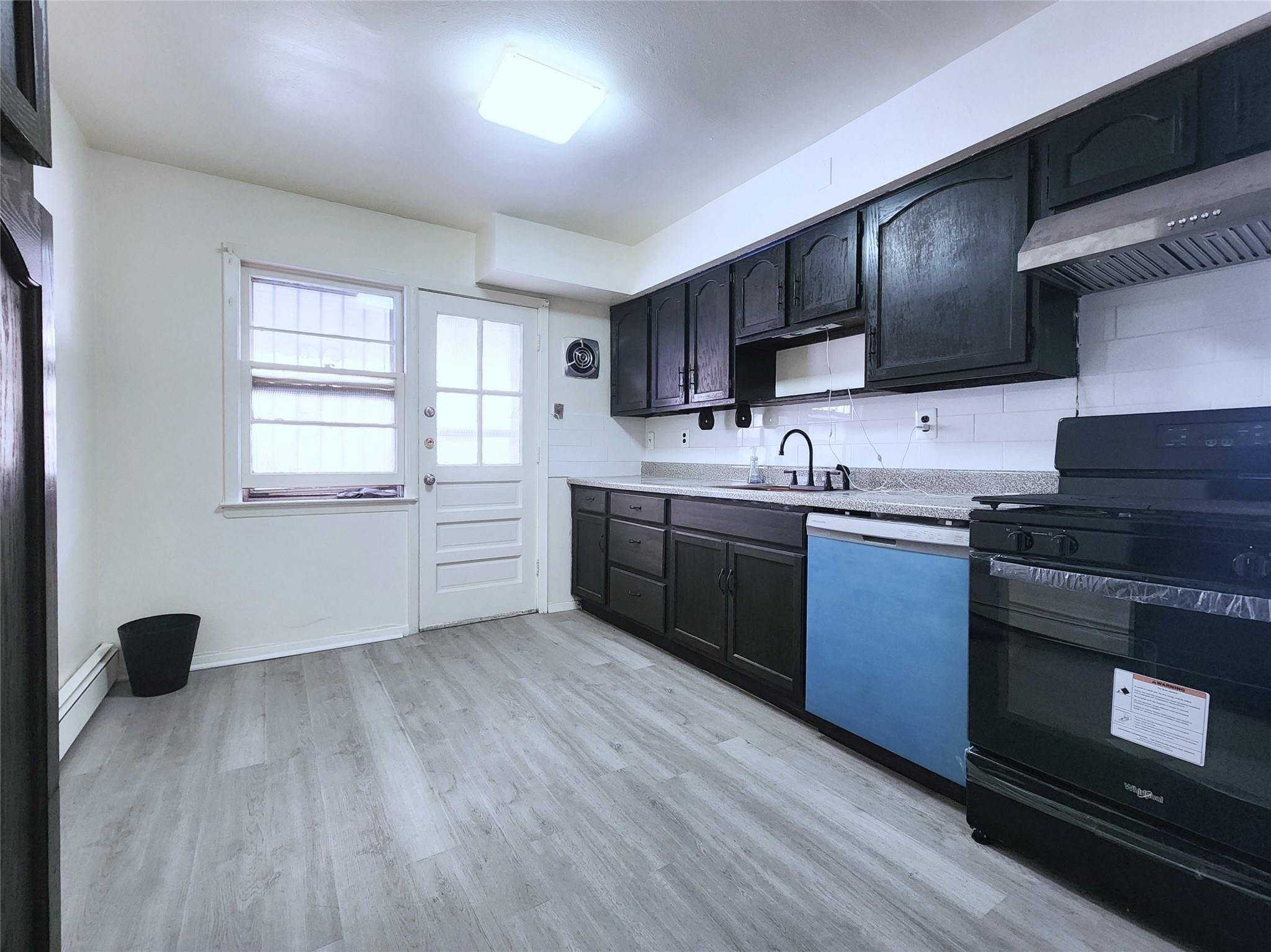 61-33 165th Street Queens, NY 11365 - Photo 2 of 11 Kitchen featuring exhaust hood, a sink, dishwashing machine, black range oven, and a baseboard heating unit