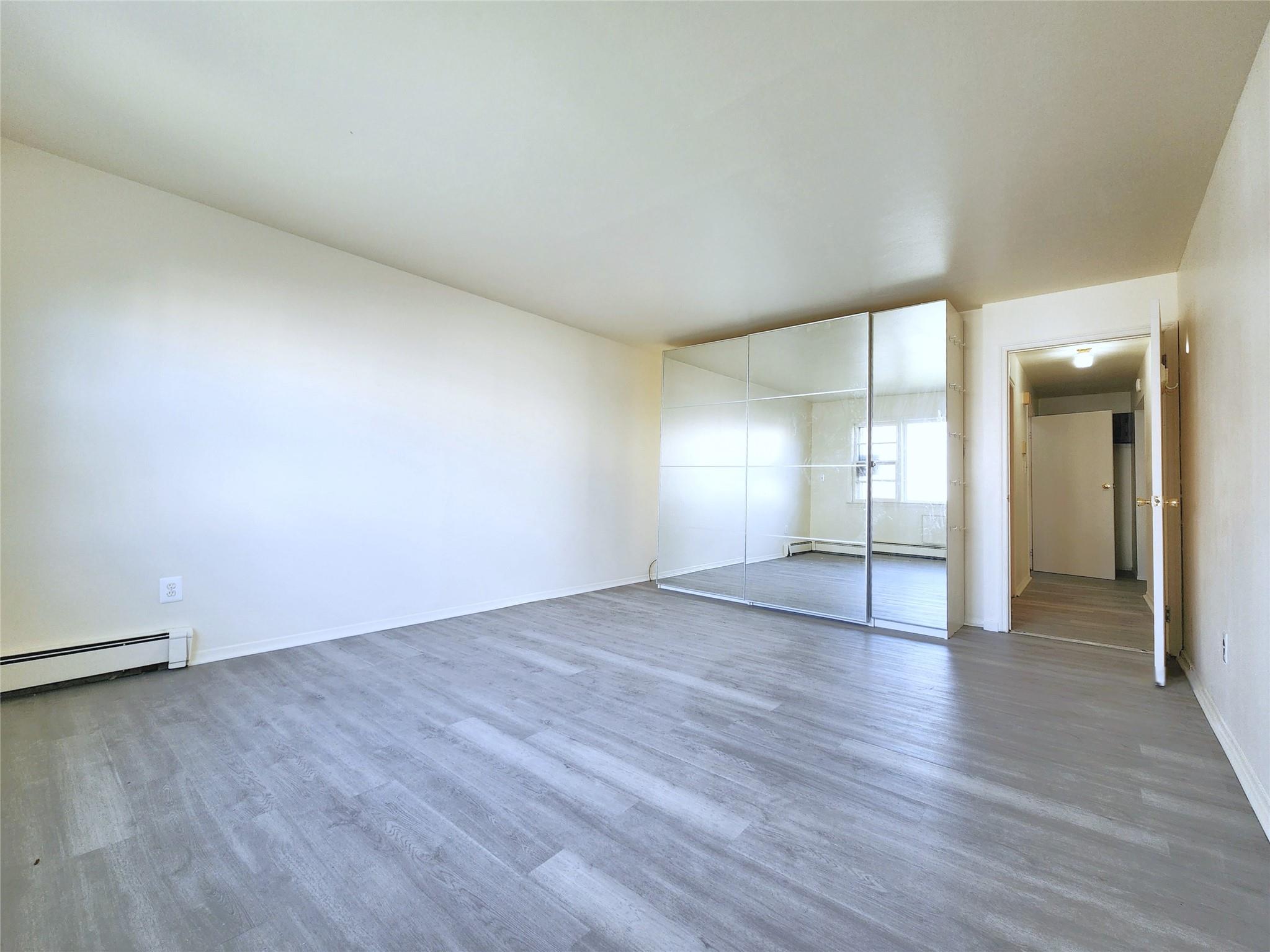 61-33 165th Street Queens, NY 11365 - Photo 5 of 11 Unfurnished bedroom featuring a baseboard radiator, wood finished floors, and baseboards