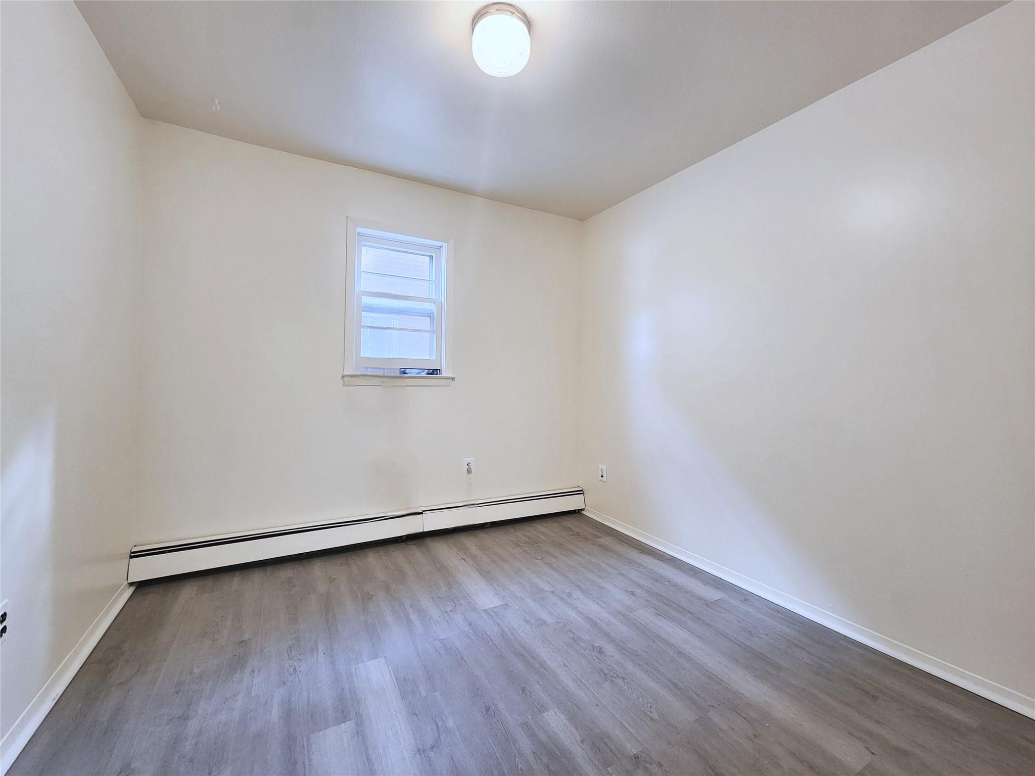 61-33 165th Street Queens, NY 11365 - Photo 10 of 11 Empty room featuring baseboards, a baseboard heating unit, and wood finished floors