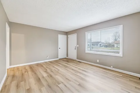 a view of an empty room with wooden floor and a window