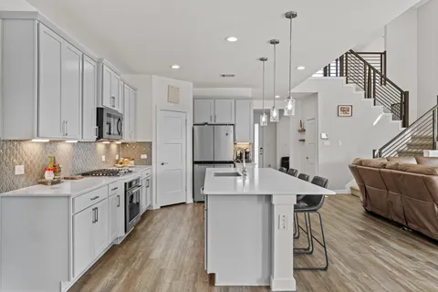 a large kitchen with stainless steel appliances kitchen island granite countertop a stove a sink a refrigerator and white cabinets with wooden floor
