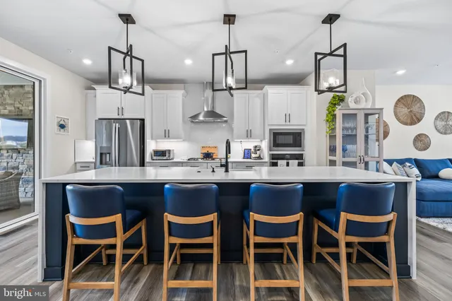 a kitchen with stainless steel appliances kitchen island granite countertop a refrigerator a stove a sink a dining table and chairs with wooden floor