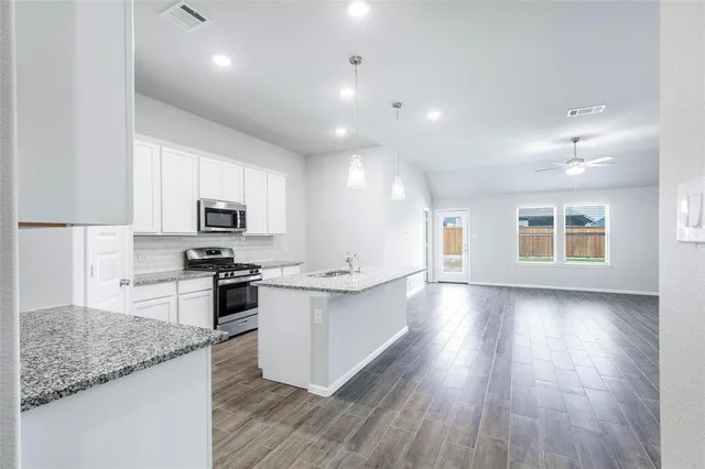 a large kitchen with stainless steel appliances kitchen island granite countertop a stove top oven a sink a dishwasher with wooden cabinets and floors