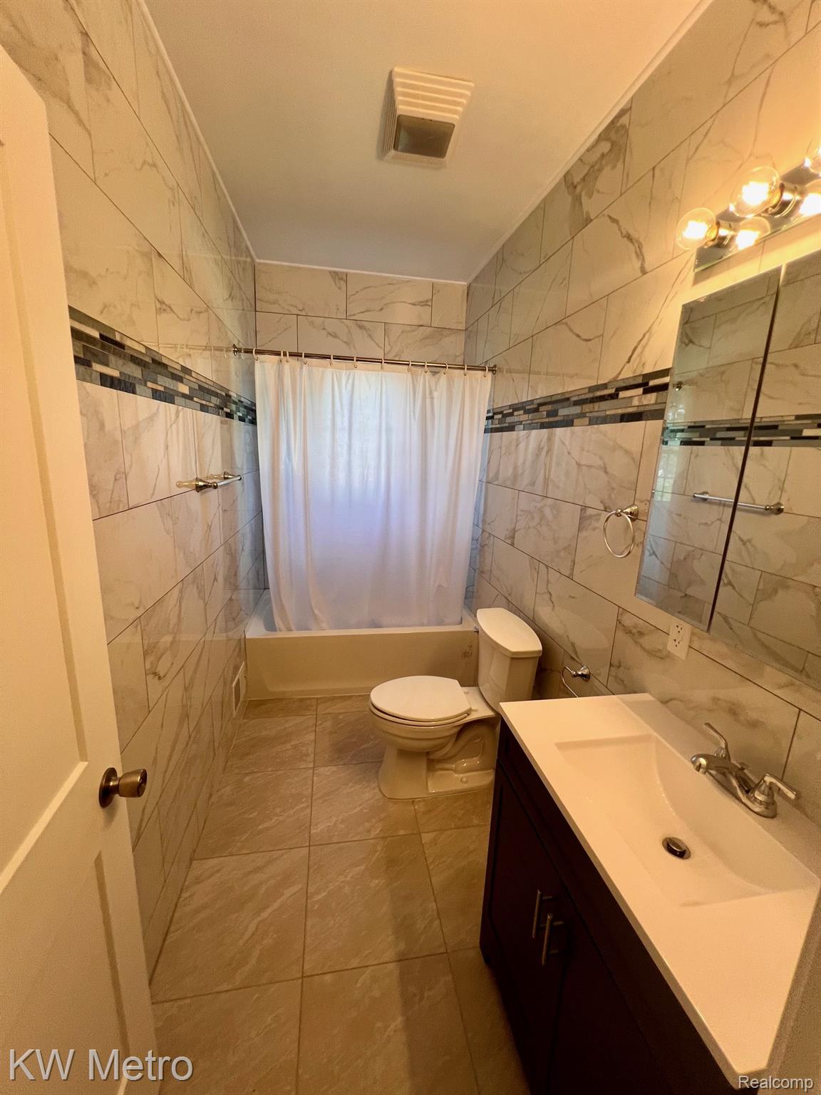 939 Webb Street Detroit, MI 48202 - Photo 13 of 19 Full bathroom featuring a tub/shower combination, tile surround with a decorative accent band, a dark wood-finish vanity with an integrated sink, and tile flooring