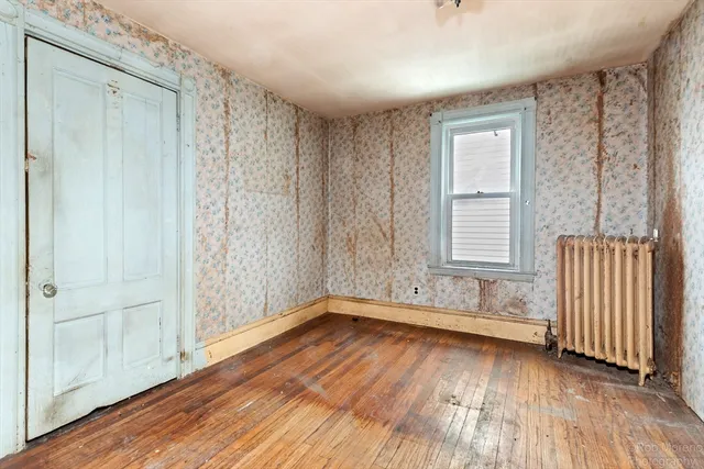 a view of an empty room with wooden floor and a window