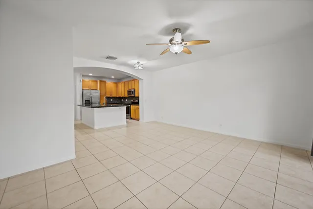 an empty room with a chandelier fan and kitchen view