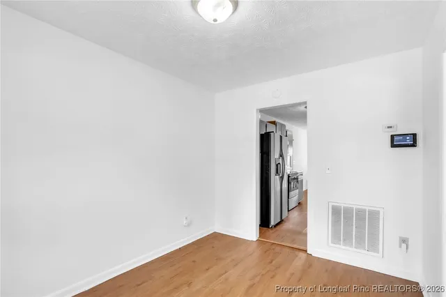 a view of an empty room with wooden floor and kitchen