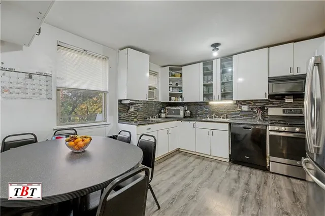 a large kitchen with stainless steel appliances a stove a sink a microwave a refrigerator and white cabinets