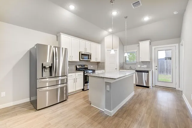a large kitchen with a center island wooden floor stainless steel appliances and windows