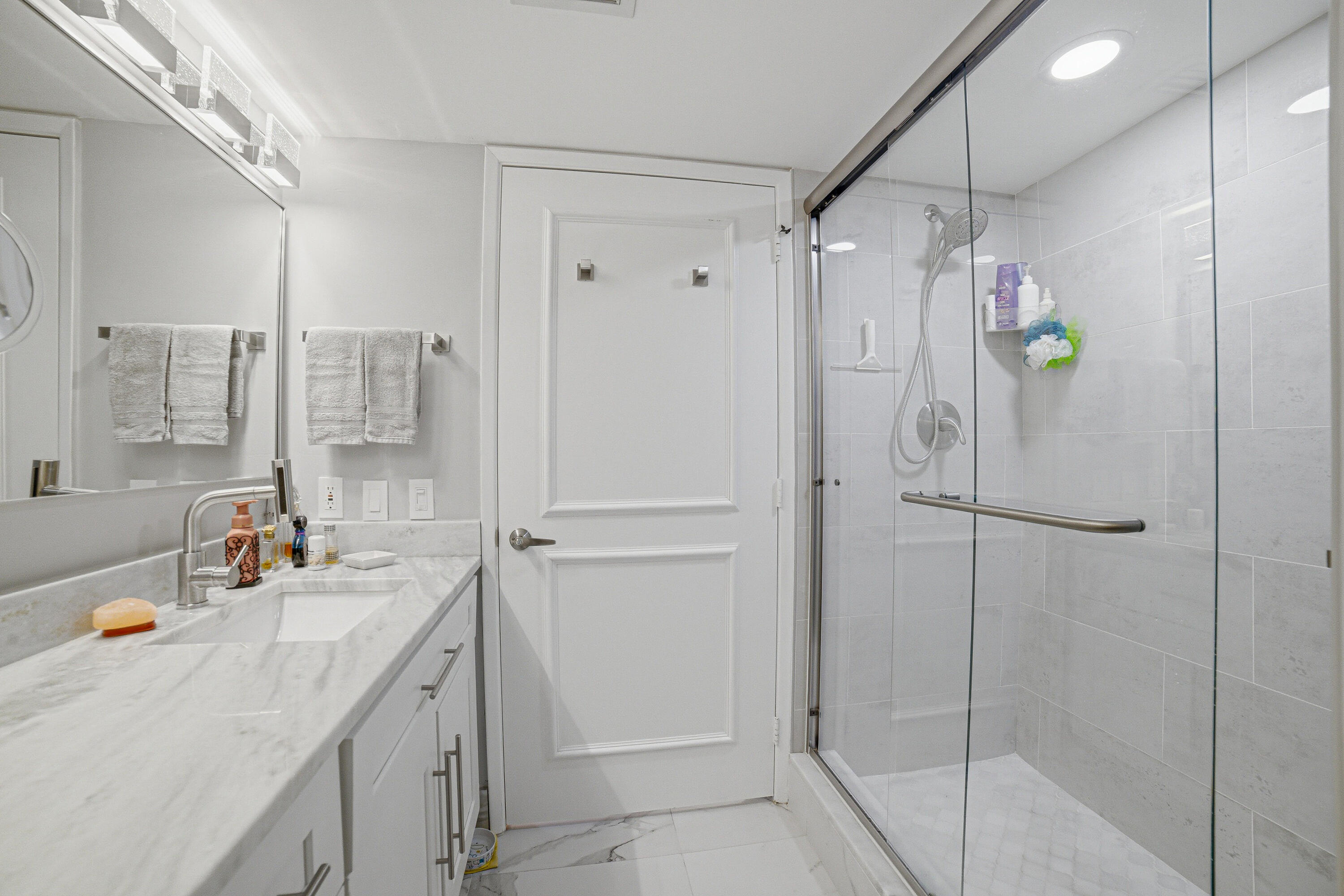 6149 Pointe Regal Circle, Unit 104 Delray Beach, FL 33484 - Photo 24 of 64 a bathroom with a shower sink vanity and mirror