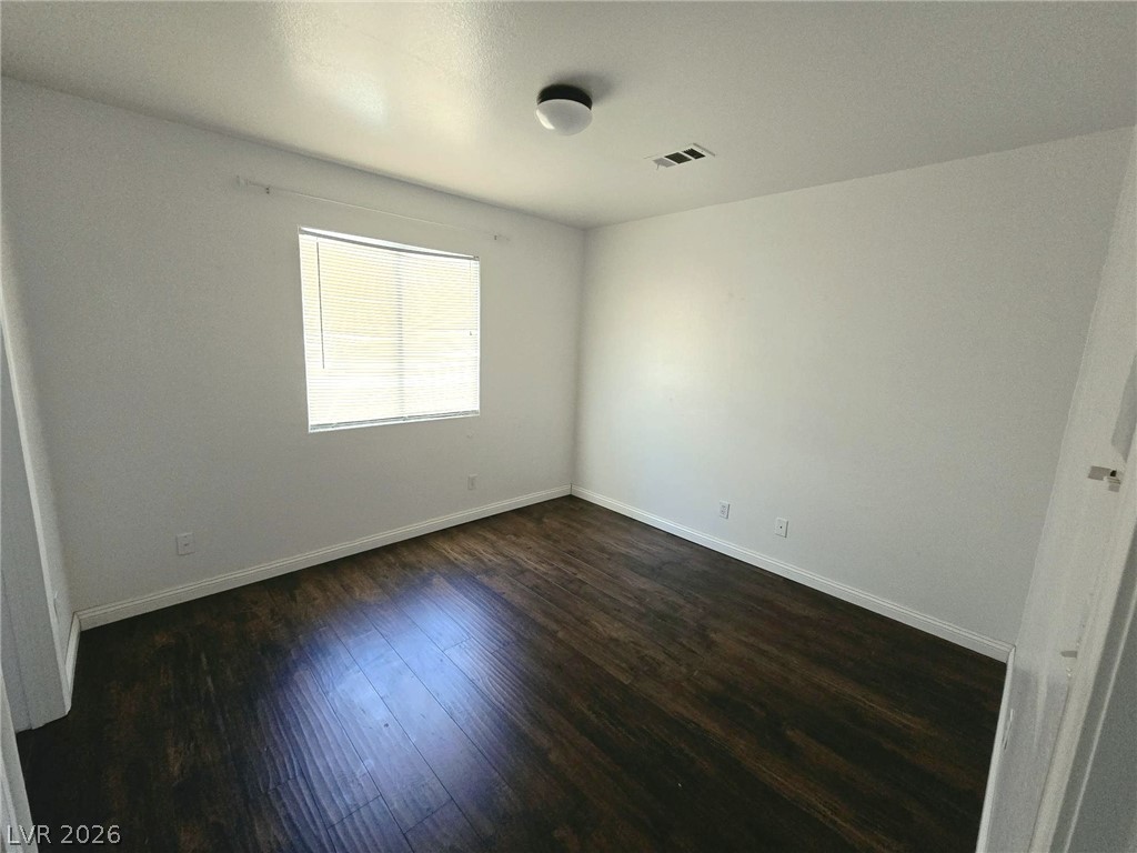 9034 West Rochelle Avenue Las Vegas, NV 89147 - Photo 6 of 8 A well-lit bedroom features rich wood flooring, crisp white walls, and a window with venetian blinds.
