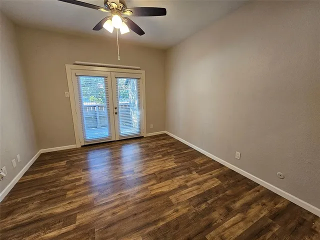 an empty room with wooden floor chandelier fan and windows