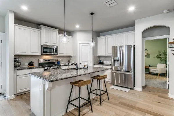 a kitchen with stainless steel appliances granite countertop a refrigerator a sink dishwasher a stove and white cabinets with wooden floor