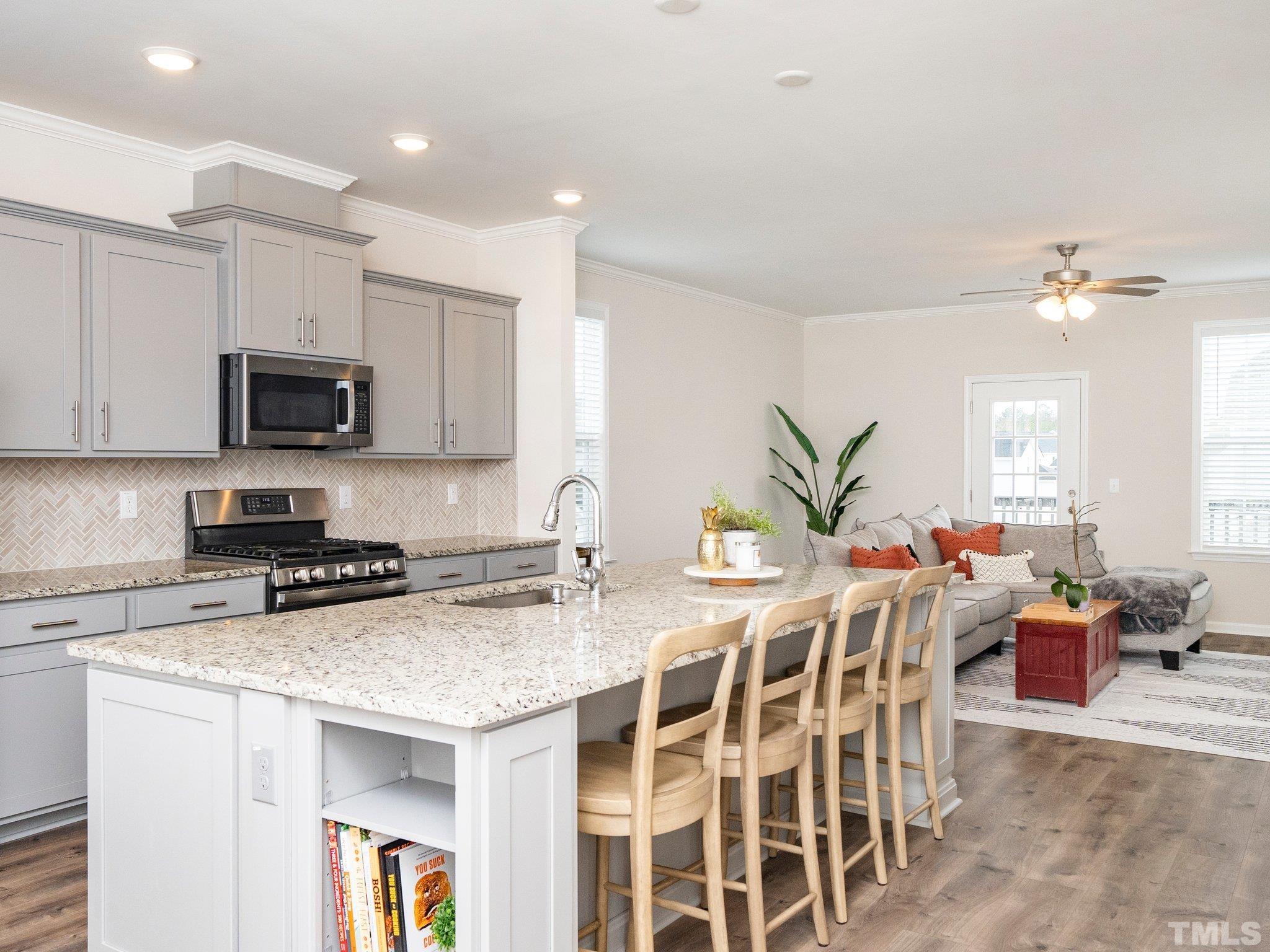 5915 Kayton Street Raleigh, NC 27616 - Photo 4 of 26 a kitchen with stainless steel appliances granite countertop a stove a sink a microwave a dining table and chairs with white cabinets