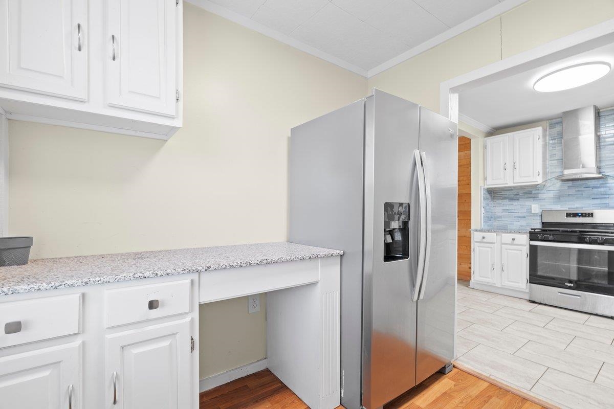 1012 Newell Road Memphis, TN 38111 - Photo 11 of 16 Kitchen with white cabinetry, decorative backsplash, ornamental molding, stainless steel appliances, and wall chimney range hood