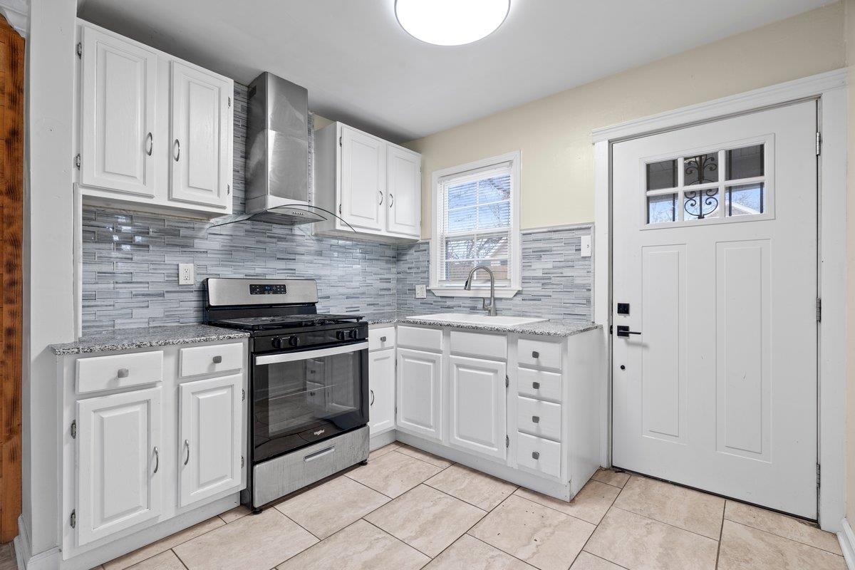 1012 Newell Road Memphis, TN 38111 - Photo 13 of 16 Kitchen featuring stainless steel gas stove, wall chimney range hood, and white cabinetry