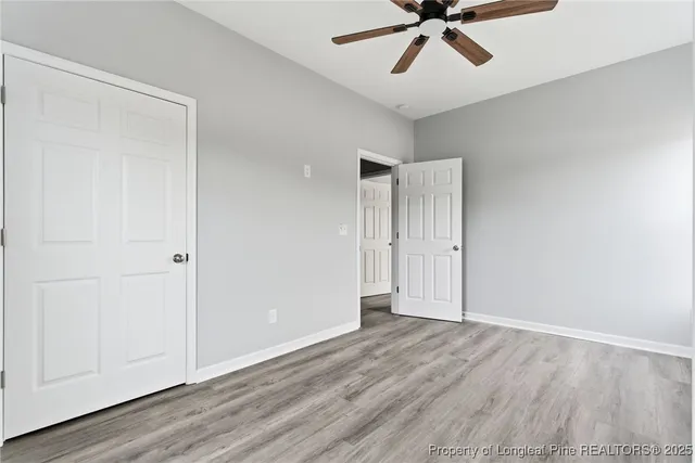 a view of an empty room with wooden floor and a ceiling fan