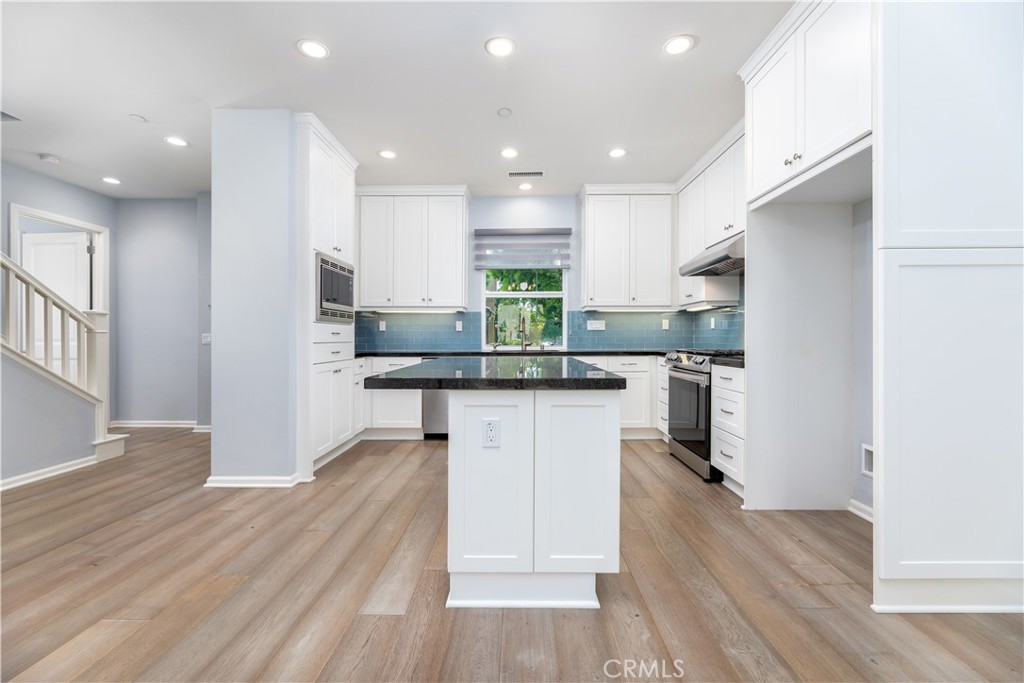 242 Firefly Irvine, CA 92618 - Photo 6 of 24 a kitchen with kitchen island granite countertop wooden floors white cabinets and stainless steel appliances