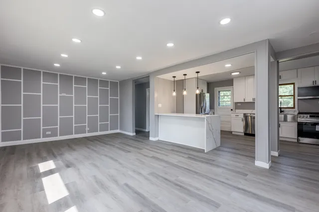 a view of an empty room with wooden floor and a kitchen