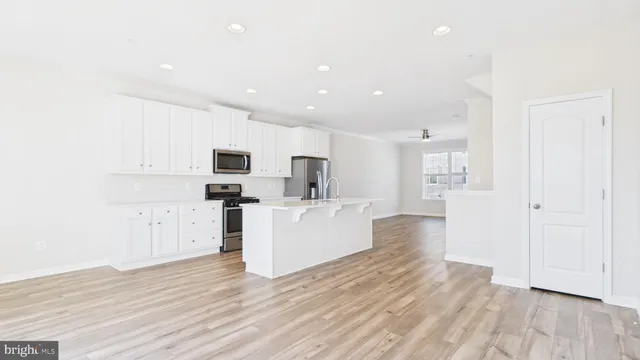 a view of kitchen with microwave a refrigerator and white cabinets with wooden floor
