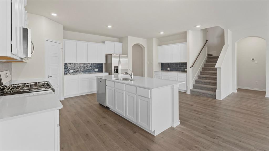 447 Epiphany Lane Lavon, TX 75166 - Photo 5 of 31 Open-concept kitchen featuring an island with an integrated sink, stainless steel appliances, white cabinetry, and wood-finish flooring