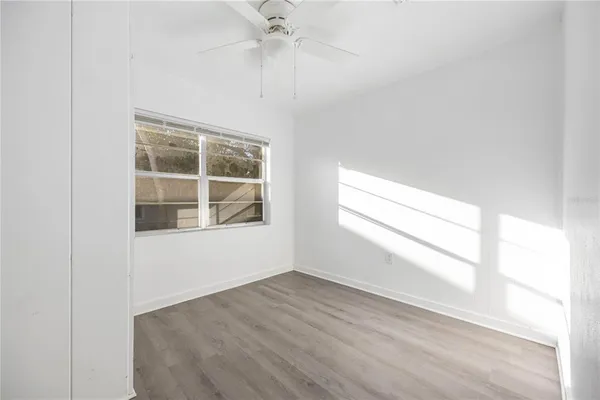 an empty room with wooden floor fan and windows
