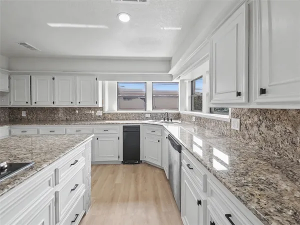 a large kitchen with granite countertop a sink dishwasher a stove and white cabinets