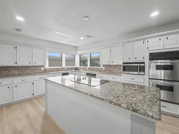 a large kitchen with granite countertop a sink and white cabinets