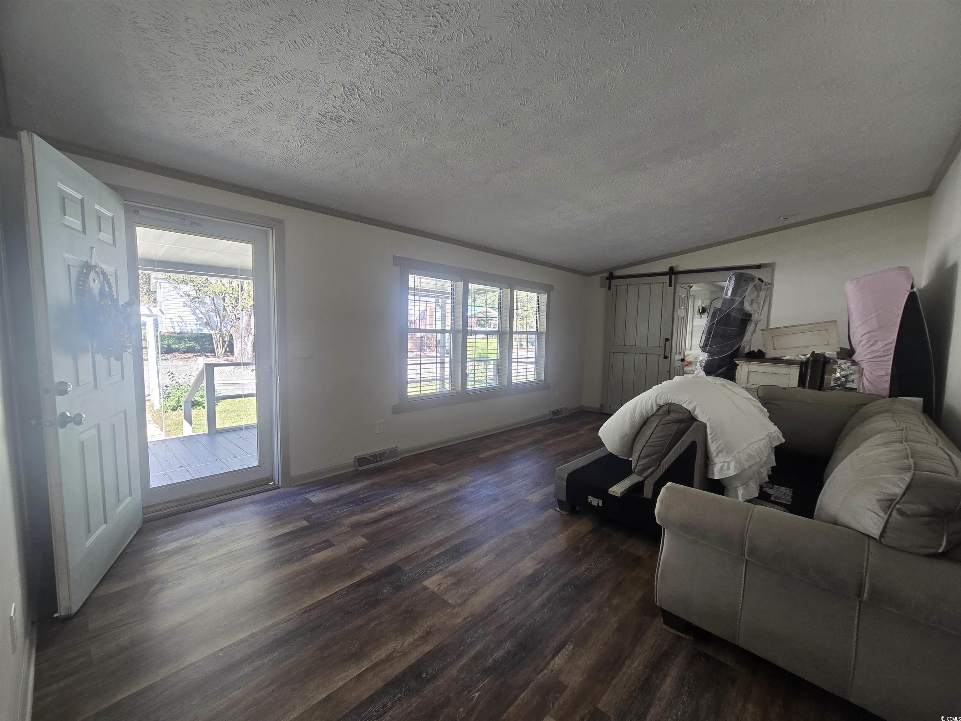 359 Lagoon Circle Murrells Inlet, SC 29576 - Photo 19 of 39 Living area with a textured ceiling, a barn door, dark wood finished floors, vaulted ceiling, and ornamental molding