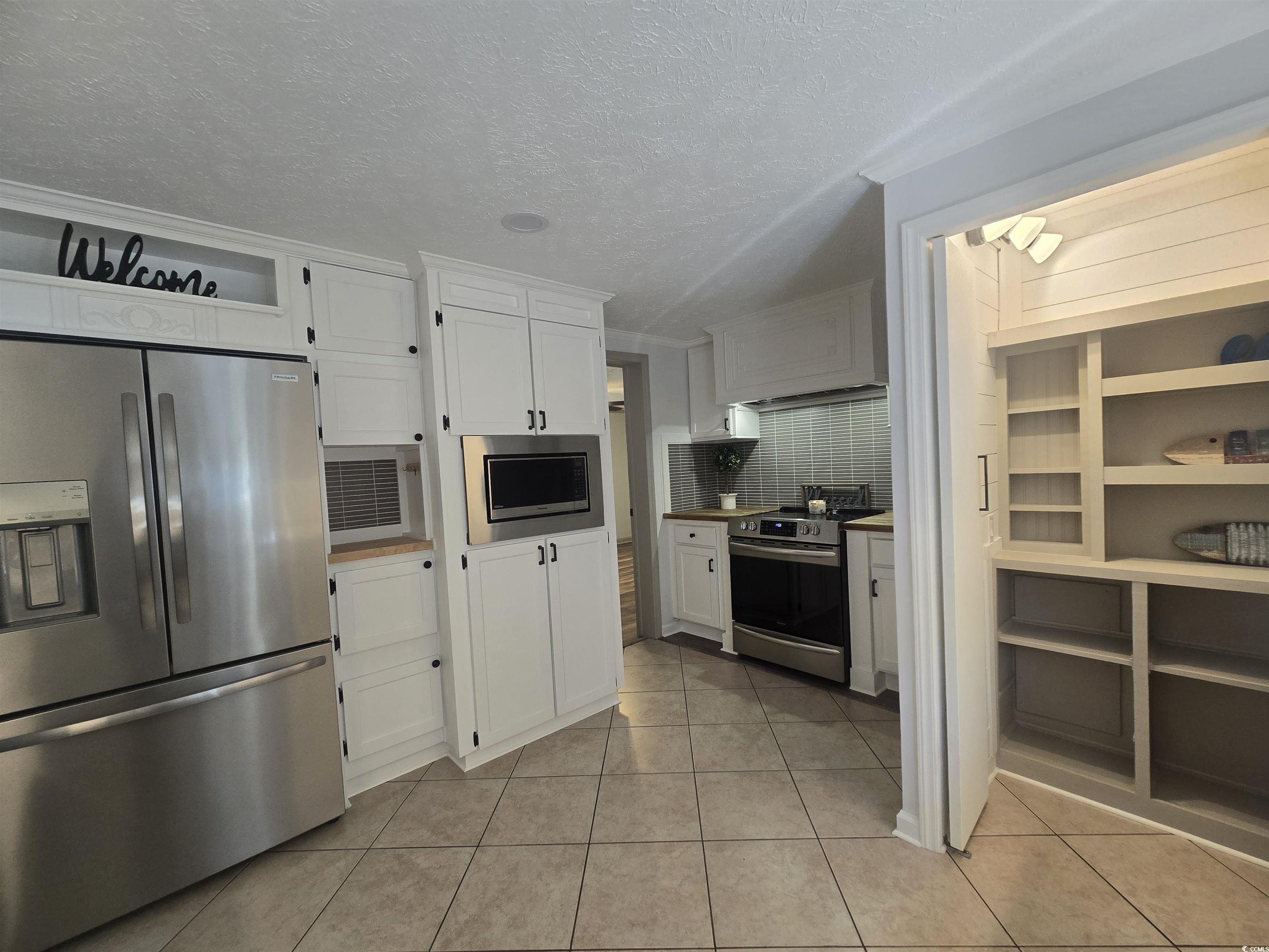 359 Lagoon Circle Murrells Inlet, SC 29576 - Photo 21 of 39 Kitchen featuring stainless steel appliances, white cabinets, light tile patterned floors, a textured ceiling, and decorative backsplash