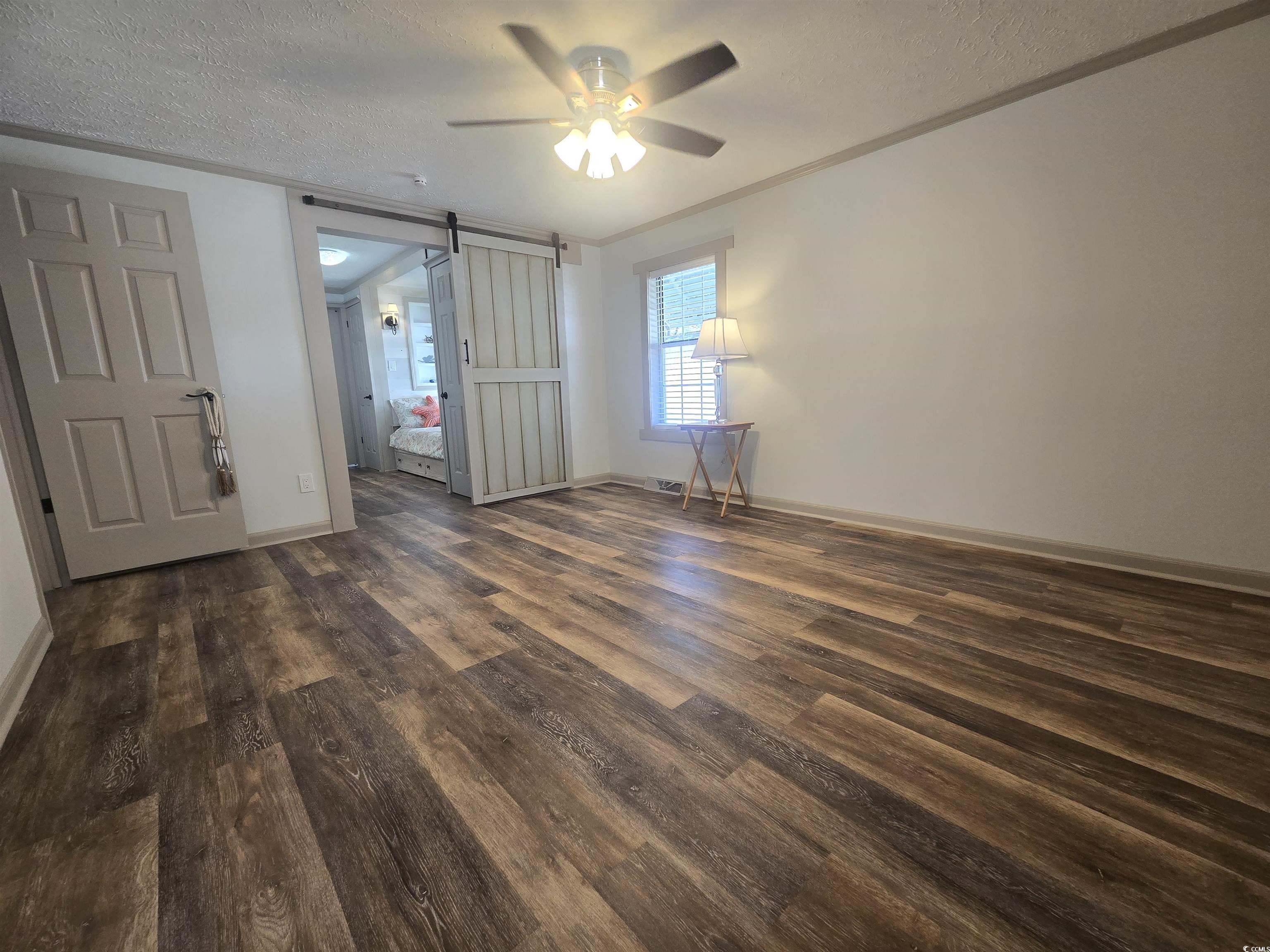 359 Lagoon Circle Murrells Inlet, SC 29576 - Photo 26 of 39 Unfurnished bedroom with a barn door, a textured ceiling, dark wood finished floors, a ceiling fan, and crown molding