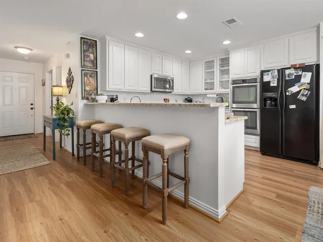 a kitchen with stainless steel appliances granite countertop a dining table chairs refrigerator and sink