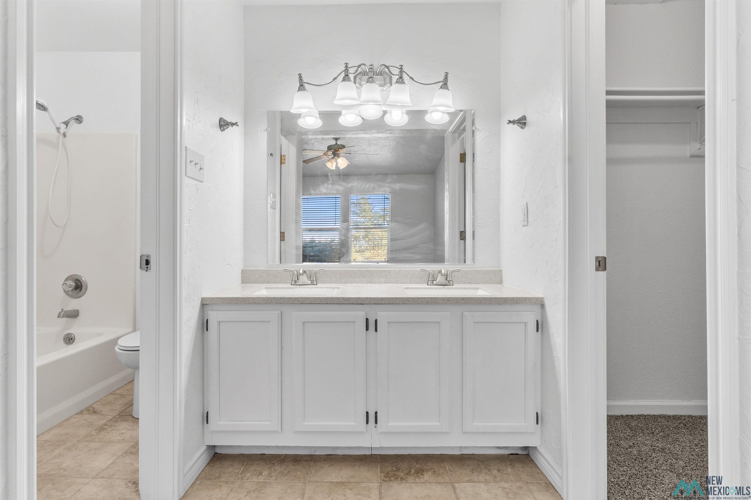 1691 County Rd K Clovis, NM 88101 - Photo 11 of 22 Bathroom with double vanity, a ceiling fan, tub / shower combination, a spacious closet, and light tile patterned floors