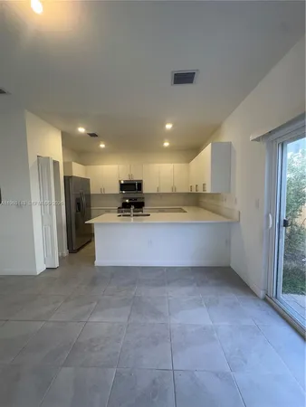 a large white kitchen with stainless steel appliances kitchen island granite countertop a refrigerator and a sink