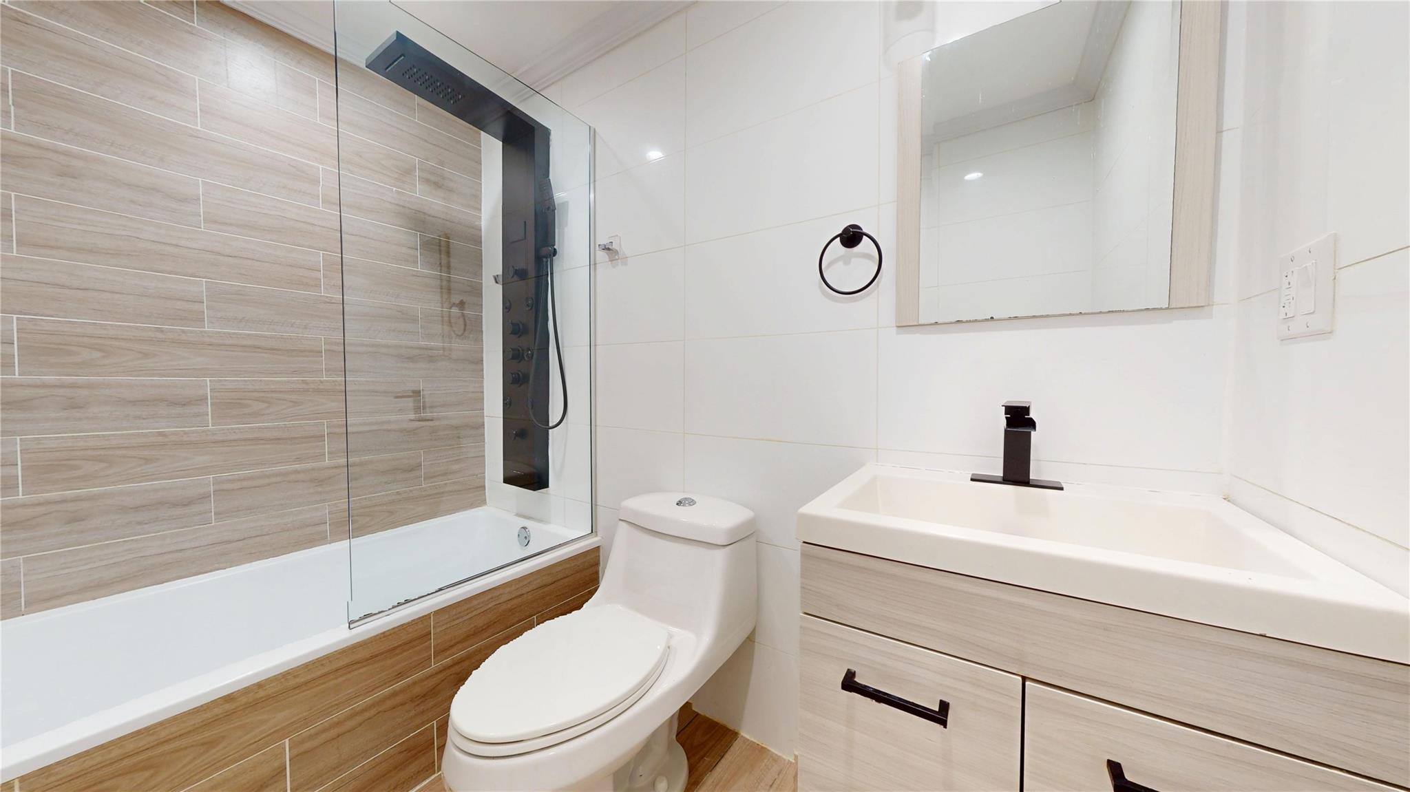 235 Sumpter Street Brooklyn, NY 11233 - Photo 5 of 7 Bathroom featuring tiled shower / bath, vanity, tile walls, and toilet
