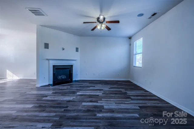 a view of an empty room with wooden floor a fireplace and a window