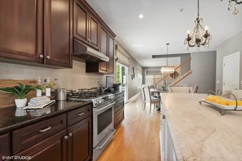 a kitchen with stainless steel appliances granite countertop a sink a stove and chairs with wooden floor