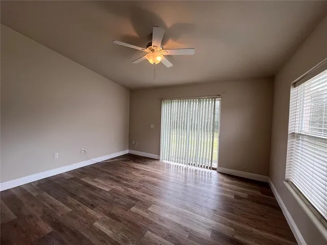 an empty room with wooden floor fan and windows