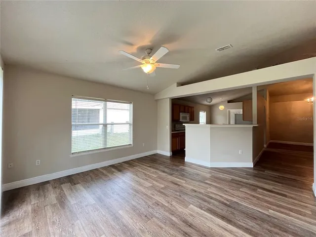 an empty room with wooden floor chandelier fan and windows