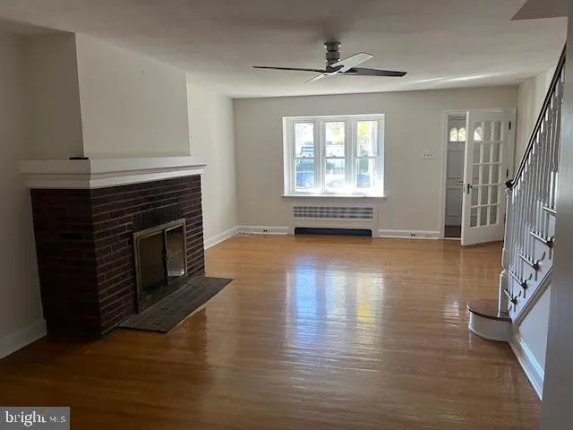 a view of an empty room with wooden floor fireplace and a window