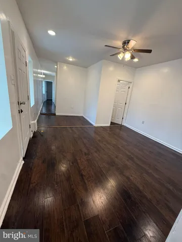 a view of an empty room with wooden floor and fan
