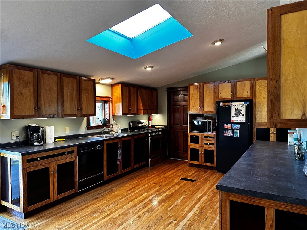 4944 Higley Road Rome, OH 44085 - Photo 8 of 28 Kitchen with light hardwood / wood-style floors, black appliances, vaulted ceiling with skylight, and sink