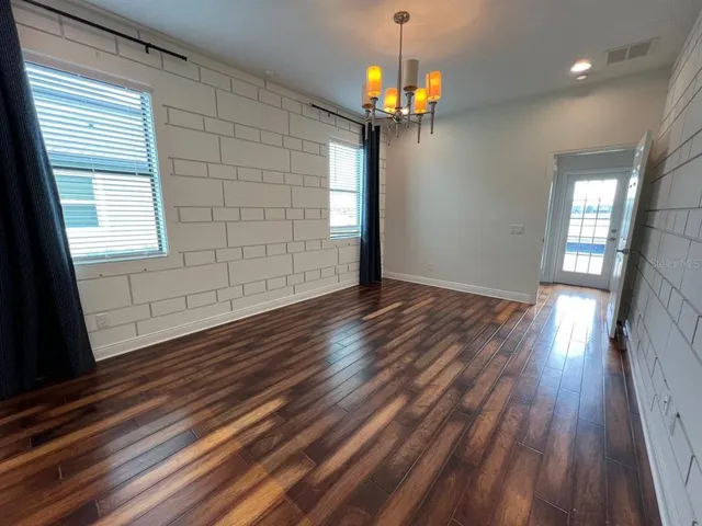 an empty room with wooden floor chandelier and windows